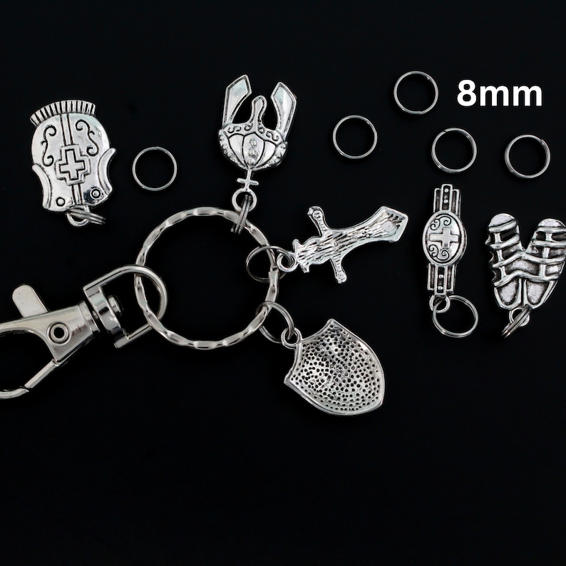 May include: A silver key chain with a variety of charms, including a sword, shield, crown, and helmet. The key chain also includes a silver clasp and several 8mm silver jump rings.