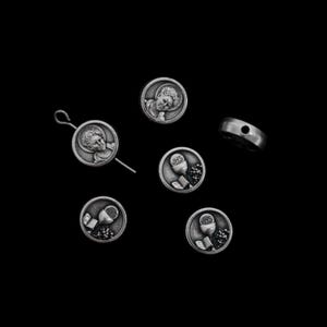 May include: A selection of silver religious charms and beads on a black backdrop. The charms display detailed images of a young person and chalices with grapes. One charm is attached to a pin.