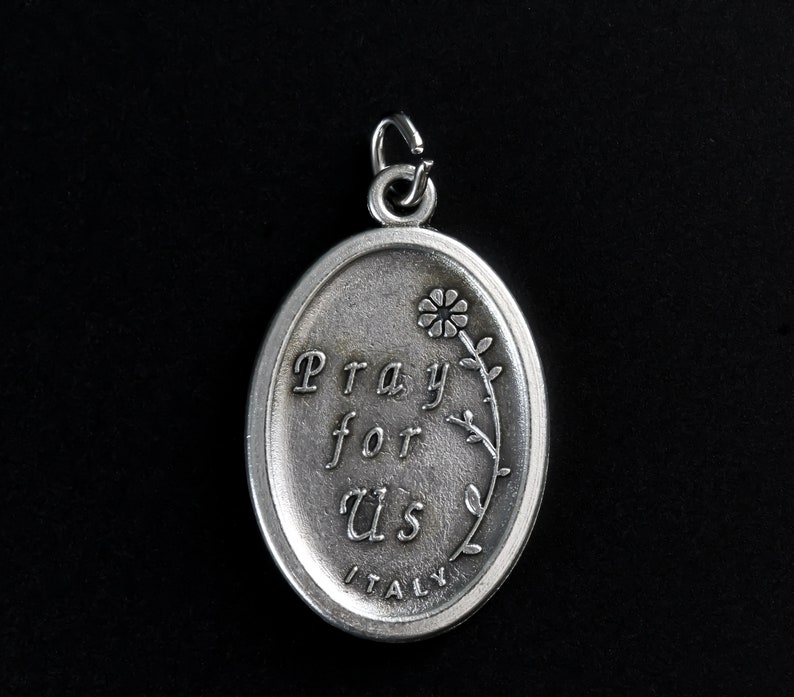 Op de afbeelding: Zilveren ovale hanger met een bloemmotief en de woorden "Pray for Us" en "ITALY" gegraveerd op de voorkant.