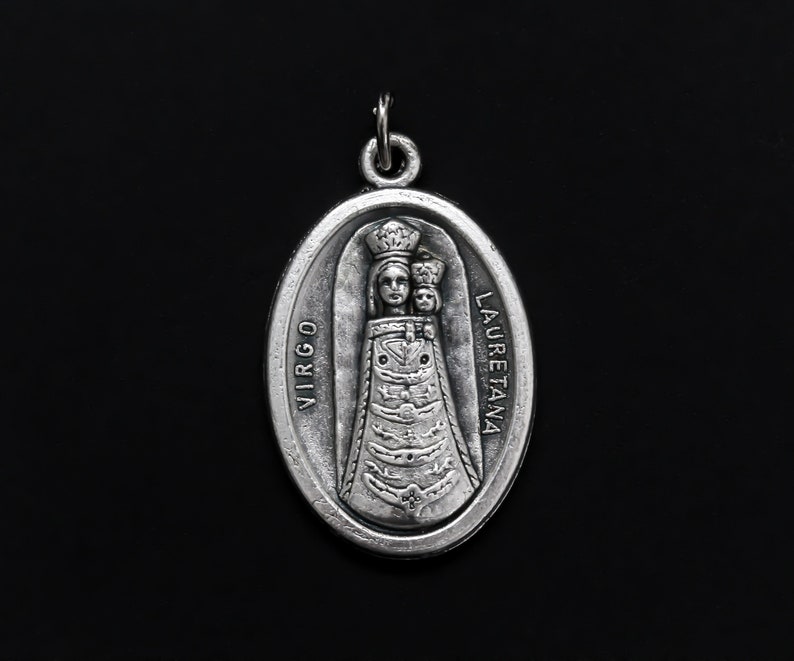 May include: Silver oval pendant with a depiction of the Virgin Mary and child. The pendant has the words "VIRGO LAURETANA" inscribed on it.