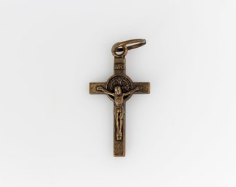 May include: A bronze-colored metal crucifix pendant with a figure of Jesus Christ on the cross. The pendant has a small loop at the top for attaching to a chain.