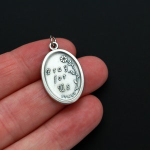 May include: Silver oval pendant with the words "Pray for Us" and a small flower design. The pendant is made in Italy.