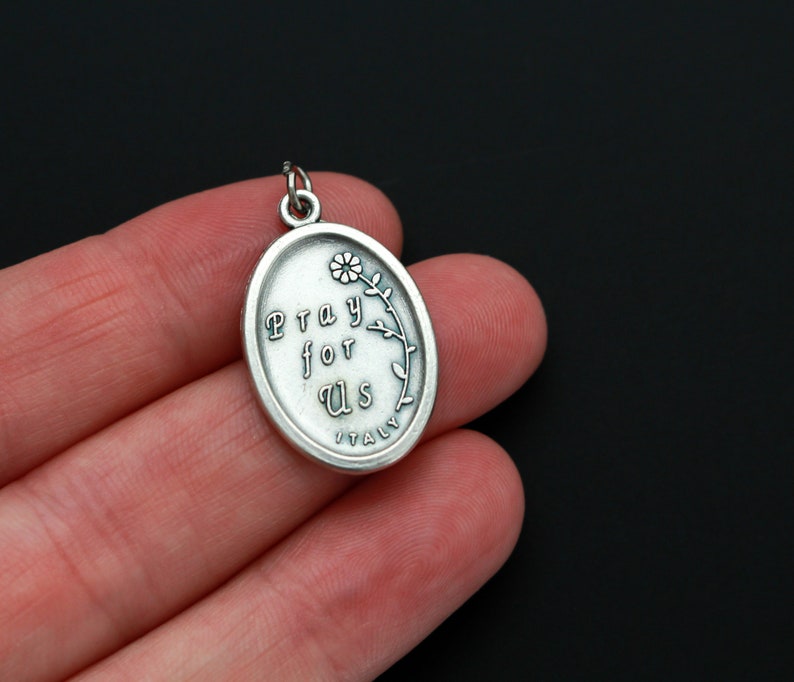 May include: Silver oval pendant with the words "Pray for Us" and a small flower design. The pendant is made in Italy.