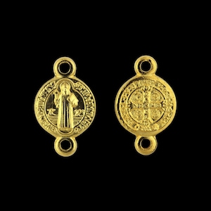 May include: Two gold-toned Saint Benedict medals with a double loop connector. One medal features a depiction of Saint Benedict and the other features a cross with the words "EGO VOX CLAMANS IN DESERTO" around the edge.