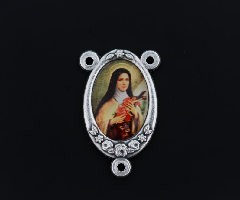 May include: Silver-toned oval-shaped pendant with a floral design. The pendant features a colorful image of Saint Th&eacute;r&egrave;se of Lisieux holding a bouquet of roses.