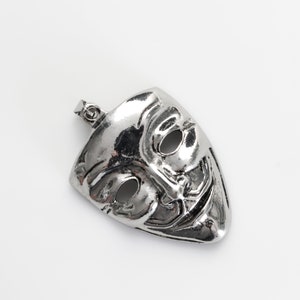 May include: A silver pendant in the shape of a mask with a mischievous grin and two black eyes. The mask is a popular symbol of anonymity and privacy.