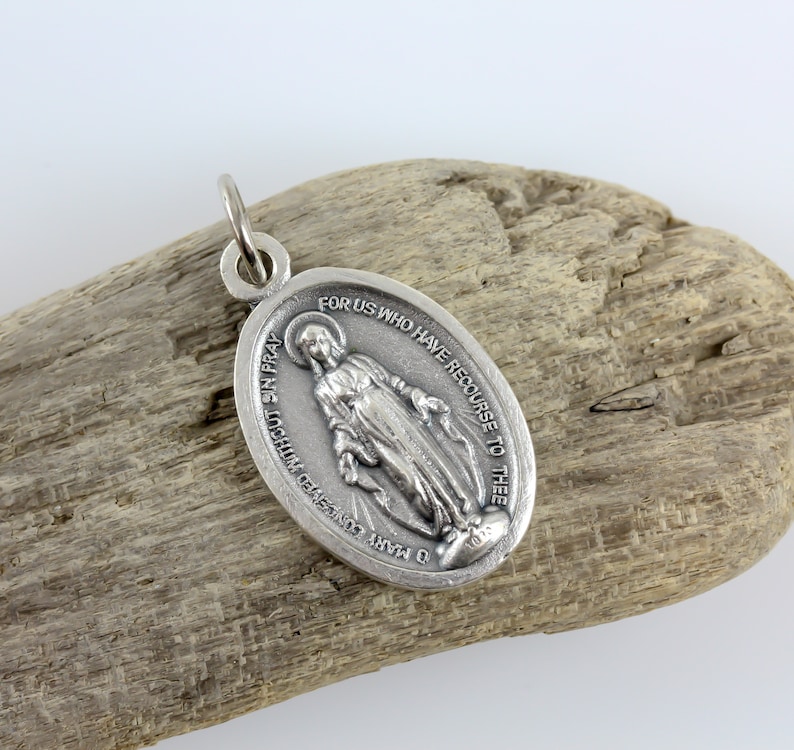 May include: Silver oval pendant with a depiction of the Virgin Mary, holding a rosary. The pendant has the inscription "O Mary conceived without sin pray for us who have recourse to thee".