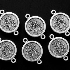 May include: Six silver-toned metal charms with a religious design. Each charm features a depiction of the Virgin Mary with a cross and the word "ITALY" printed on the bottom.
