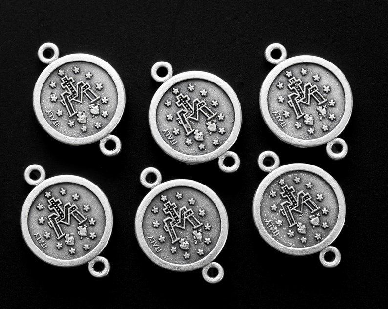 May include: Six silver-toned metal charms with a religious design. Each charm features a depiction of the Virgin Mary with a cross and the word "ITALY" printed on the bottom.