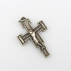 Op de afbeelding: Een zilveren metalen kruisbeeld met een gedetailleerd ontwerp. Het kruisbeeld toont een figuur van Jezus Christus aan het kruis, met twee kleinere figuren aan weerszijden. De inscriptie "INRI" is zichtbaar op het kruis.