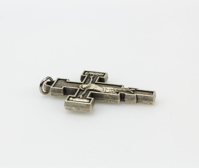 Op de afbeelding: Een zilverkleurige metalen kruis hanger met een gedetailleerde afbeelding van Jezus Christus aan het kruis.