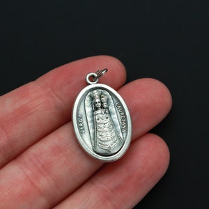 May include: Silver oval pendant with a depiction of the Virgin Mary and child. The pendant has the words "VIRGO LAURETANA" inscribed on it.