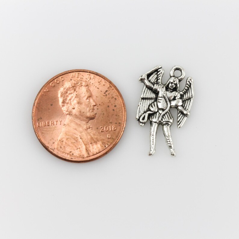 May include: Silver charm of an angel with wings outstretched, holding a sword. The charm is about the size of a US penny.