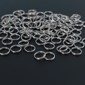May include: A large pile of silver key rings on a black surface. The key rings are all the same size and shape, and they are arranged in a random pattern.