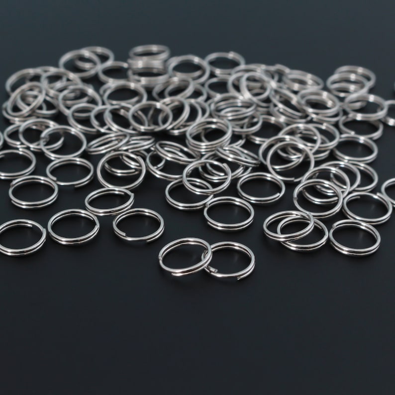 May include: A large pile of silver key rings on a black surface. The key rings are all the same size and shape, and they are arranged in a random pattern.