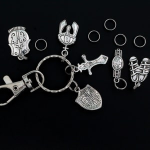 May include: A silver key chain with a variety of charms, including a shield, a sword, a helmet, and a crown. The charms are attached to a silver key ring with a silver clasp.