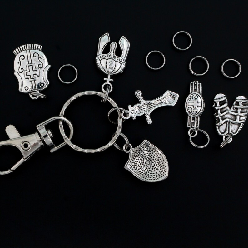 May include: A silver key chain with a variety of charms, including a shield, a sword, a helmet, and a crown. The charms are attached to a silver key ring with a silver clasp.