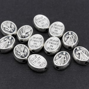 Puede incluir: Cuentas ovaladas de plata con las palabras "Jes&uacute;s, conf&iacute;o en ti" grabadas. Las cuentas presentan una imagen en relieve de una paloma con rayos de luz.