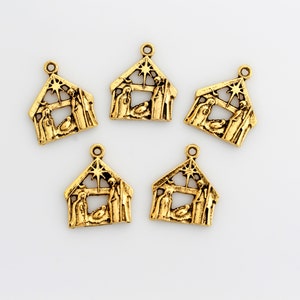 May include: Five gold-colored metal charms shaped like a nativity scene with a star on top. The charms are approximately 1 inch in size.