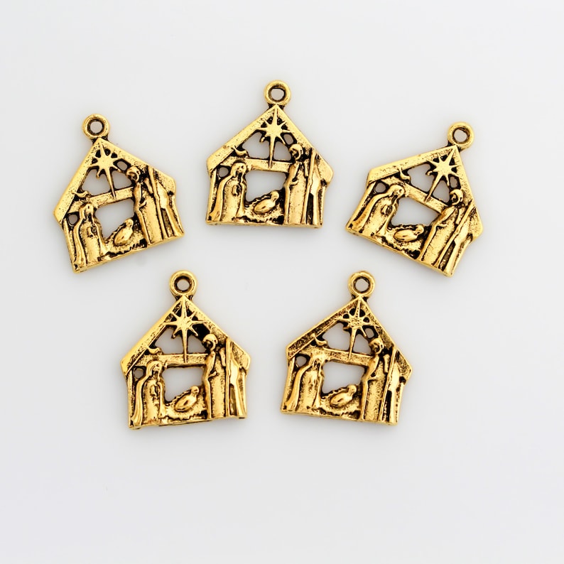 May include: Five gold-colored metal charms shaped like a nativity scene with a star on top. The charms are approximately 1 inch in size.