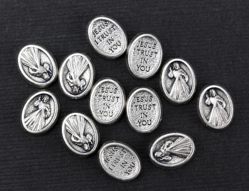 Puede incluir: Una colecci&oacute;n de dijes ovalados plateados con las palabras "Jes&uacute;s conf&iacute;o en ti" y una imagen de un coraz&oacute;n con rayos de luz.