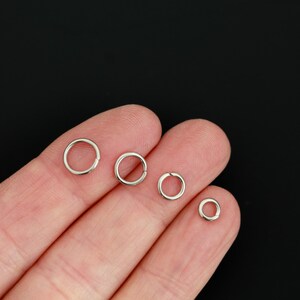 K&ouml;nnte beinhalten: Vier silberfarbene Metall-Biegeringe in verschiedenen Gr&ouml;&szlig;en, die in einer Reihe angeordnet sind. Jeder kreisf&ouml;rmige Ring weist eine kleine, deutliche &Ouml;ffnung entlang seines Umfangs auf, um Schmuckkomponenten oder andere kleine Bastelartikel sicher zu verbinden.