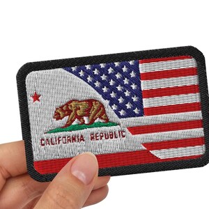 Puede incluir: Un parche rectangular bordado que presenta un diseño híbrido que combina la bandera del estado de California con un oso pardo y una estrella roja a la izquierda, y la bandera de los Estados Unidos con estrellas azules y rayas rojas y blancas a la derecha.