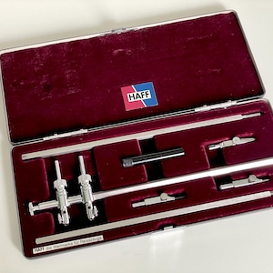 May include: A silver HAFF drafting instrument set housed in a rectangular metal case with a deep burgundy velvet interior. The set includes various metal compass components and extensions. The case features a HAFF logo and text label.