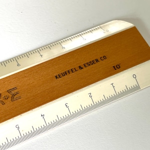 May include: A vintage Keuffel & Esser Co. ruler with a wooden center and white edges. The ruler is marked with both inch and centimeter measurements. The text "KEUFFEL & ESSER CO" and "10" are visible.