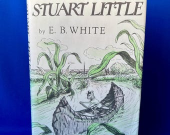 May include: A hardback book titled Stuart Little by E. B. White with illustrations by Garth Williams. The cover features a line drawing of a mouse paddling a canoe labelled Summer Memories through a river surrounded by tall green plants.