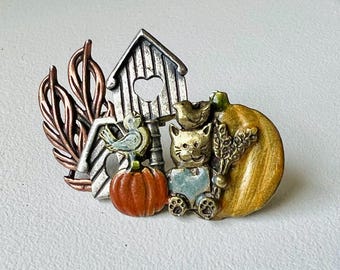 May include: A detailed metal brooch featuring autumn-themed elements. It includes a birdhouse with a heart-shaped cutout, a pumpkin, a cat wearing overalls, a bird, and wheat. The brooch has copper, silver, and gold tones.