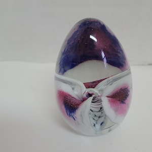 May include: A white glass paperweight with a swirling pattern of pink and blue.