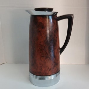 May include: A vintage brown and silver thermos with a dark handle and lid. The thermos has a wood-grain pattern and a silver base. The handle is dark brown, and the lid is black with a white rim. The thermos is approximately 30 cm tall.