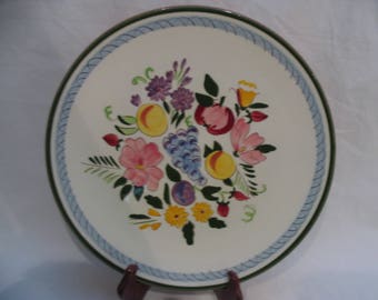 May include: A white ceramic plate with a green and blue rim features a hand-painted floral design with pink, yellow, purple, and green flowers and fruit.