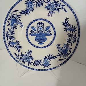 Puede incluir: Un plato de cerámica blanco con un diseño floral azul y blanco. El plato tiene un borde festoneado y un diseño central en relieve.