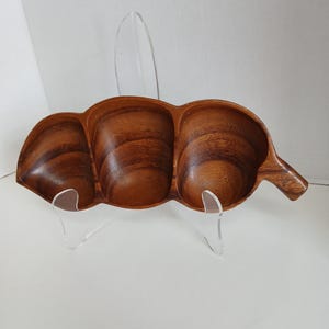 Könnte beinhalten: Eine Servierplatte aus Holz mit drei Abschnitten, geformt wie ein Blatt. Die Platte ist aus dunkelbraunem Holz mit natürlicher Maserung. Sie hat einen Griff auf einer Seite und steht auf einem klaren Acryl-Ständer.
