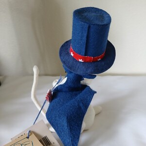 Peut inclure: Figurine de chat blanc portant un chapeau bleu en feutre de l'Oncle Sam avec une bande rouge orn&eacute;e d'&eacute;toiles blanches. Le chat porte &eacute;galement une cape bleue. Une &eacute;tiquette est attach&eacute;e au chat.
