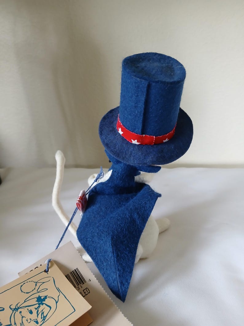Peut inclure: Figurine de chat blanc portant un chapeau bleu en feutre de l'Oncle Sam avec une bande rouge orn&eacute;e d'&eacute;toiles blanches. Le chat porte &eacute;galement une cape bleue. Une &eacute;tiquette est attach&eacute;e au chat.
