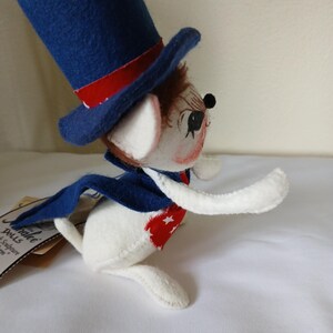 Peut inclure: Poup&eacute;e souris patriotique, v&ecirc;tue d'un haut-de-forme bleu avec une bande rouge, d'une cape bleue et d'un gilet &agrave; motifs d'&eacute;toiles rouges et blanches. La poup&eacute;e a un corps blanc, des cheveux bruns et un visage peint.