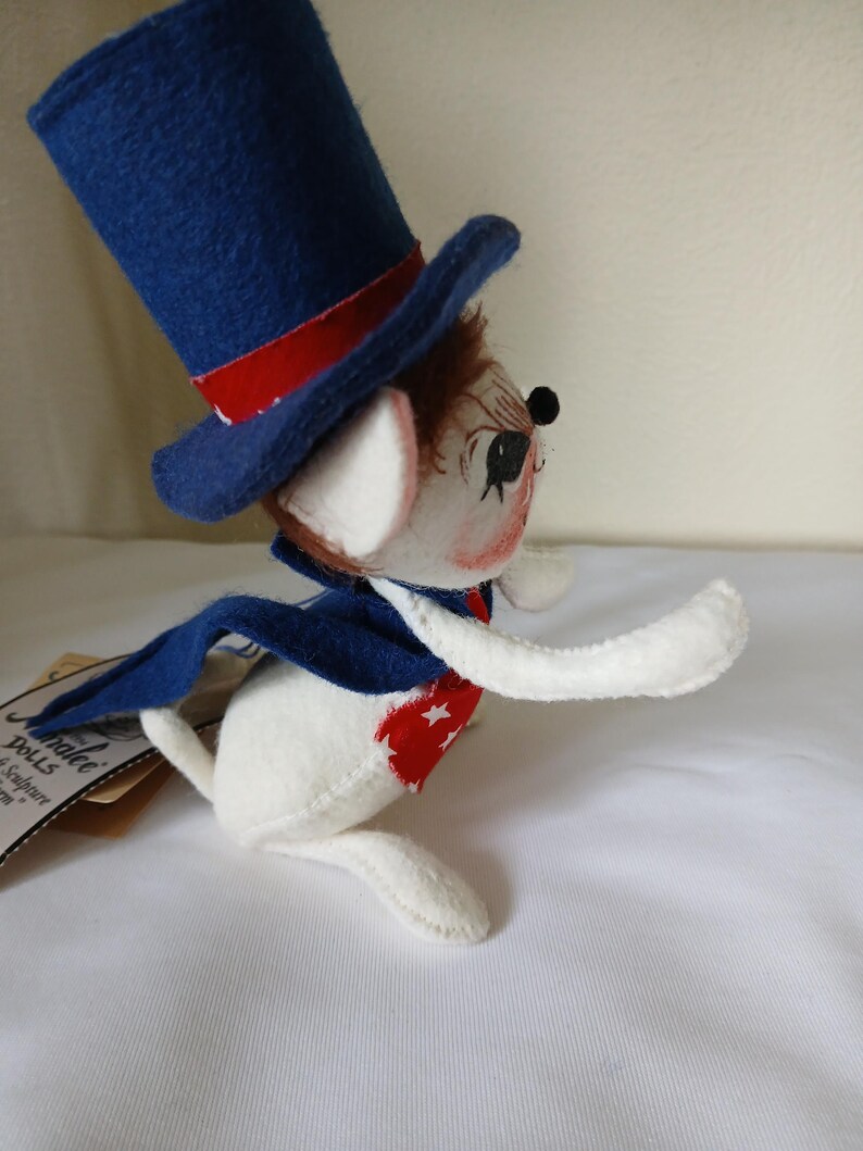 Peut inclure: Poup&eacute;e souris patriotique, v&ecirc;tue d'un haut-de-forme bleu avec une bande rouge, d'une cape bleue et d'un gilet &agrave; motifs d'&eacute;toiles rouges et blanches. La poup&eacute;e a un corps blanc, des cheveux bruns et un visage peint.