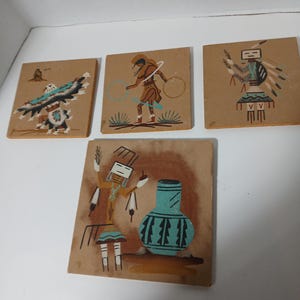 Può includere: Quattro piastrelle quadrate dipinte con sabbia con disegni nativi americani. Le piastrelle raffigurano figure, un'aquila e un vaso nei toni della terra del marrone, blu e bianco. L'opera d'arte è su uno sfondo beige.