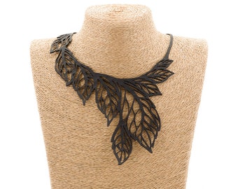 May include: A black leather necklace with a delicate, leafy design. The necklace is displayed on a brown mannequin bust.