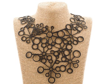 May include: A black leather necklace with a geometric design featuring interconnected circles and lines. The necklace is displayed on a brown mannequin bust.