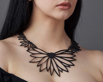 May include: A black, intricate, laser-cut necklace with a floral design. The necklace is made of multiple layers of delicate, overlapping petals.
