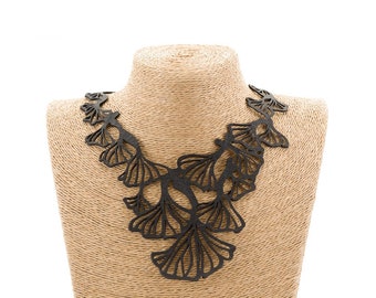 May include: A black leather necklace with a delicate, intricate design of leaves. The necklace is displayed on a brown mannequin bust.