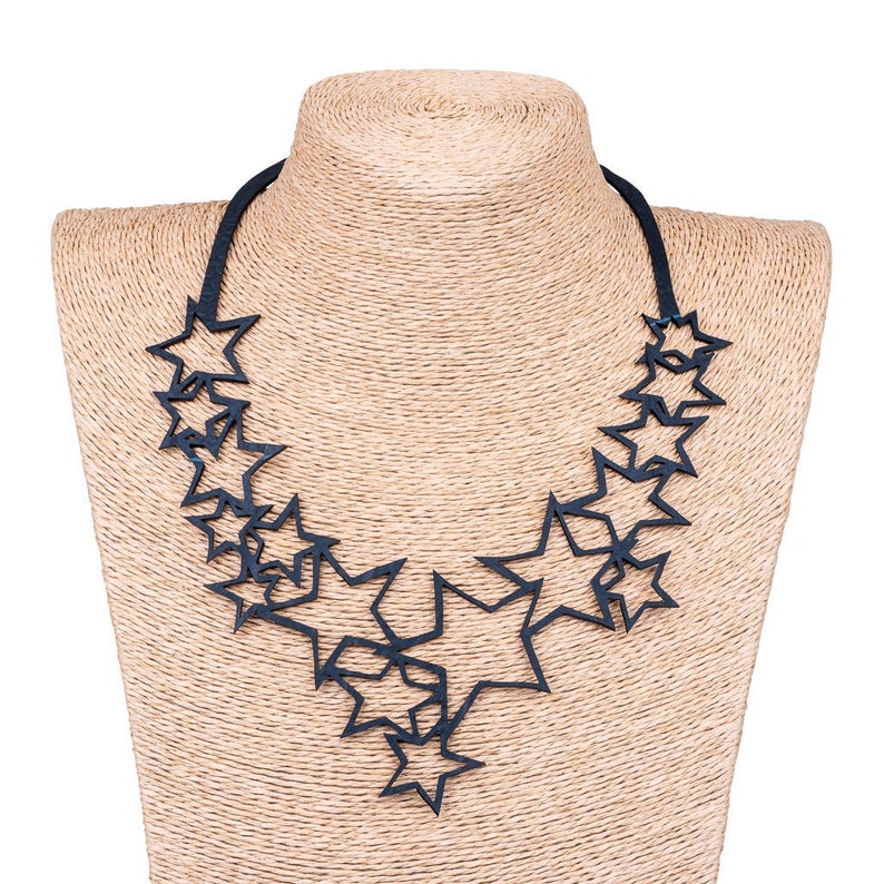 May include: A black necklace made of layered star shapes. The necklace is displayed on a tan mannequin bust.