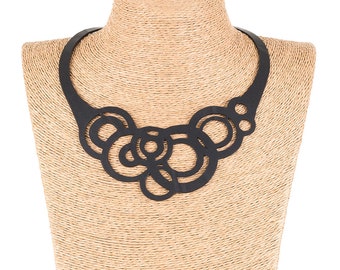 May include: A black necklace made of layered circles, worn on a straw-colored mannequin.