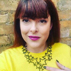 May include: A woman wearing a yellow sweater with a large green star-shaped necklace.