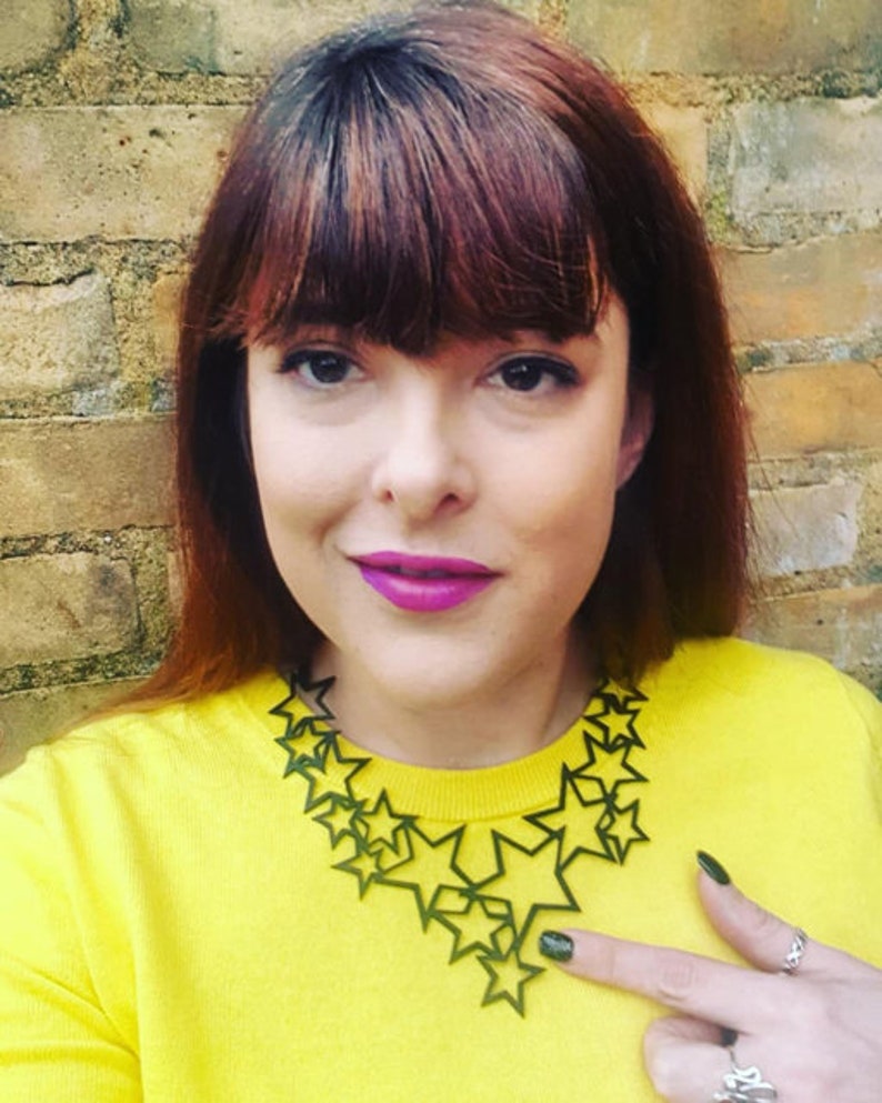 May include: A woman wearing a yellow sweater with a large green star-shaped necklace.