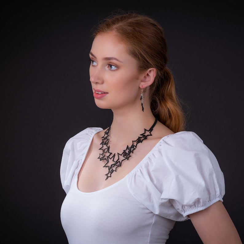 May include: A woman with red hair wearing a white blouse with a black star-shaped necklace and earrings.